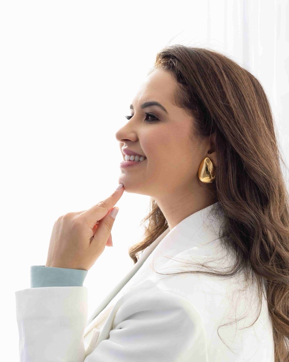 Dra. Daniela Vargas de perfil, com a mão no queixo, em ambiente de luz natural